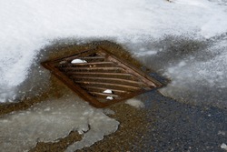 An image of an old rusted metal storm drain lid with melting snow. 