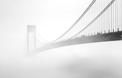 Black and white image of a bridge hidden in the fog. The Verrazano-Narrows Bridge is a double-decked suspension bridge that connects the New York City boroughs of Staten Island and Brooklyn