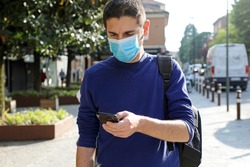 COVID-19 Pandemic Coronavirus Worried Young Man Wearing Surgical Mask Using Smart Phone App in City Street to Aid Contact Tracing and Self Diagnostic in Response to the Coronavirus Pandemic 2019