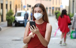 COVID-19 Woman in city street wearing KN95 FFP2 mask against disease virus SARS-CoV-2 and using Smart Phone App to aid contact tracing and self diagnostic in response to Coronavirus Disease 2019