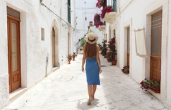 Back view of young tourist woman on ancient street in old town. Travel woman in straw hat and blue dress enjoying vacation in Europe. Tourism and travel concept.