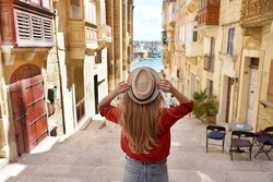 Tourism in Malta. Back view of tourist girl holding hat descends stairs in the old town of Valletta, UNESCO World Heritage, Malta.