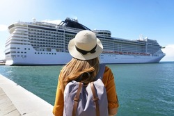 Cruise vacation. Rear view of tourist girl with backpack and hat standing in front of big cruise ship.