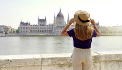Tourism in Europe. Back view of young woman with hat enjoying view of  Hungarian Parliament Building on Danube River in Budapest, Hungary.