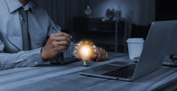 Hand of businessman holding a pen to go at illuminated light bulb with network connection line, idea, innovation and inspiration concept. concept creativity with bulbs that shine glitter.