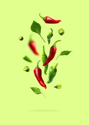 Flying green and red chili pepper, leaves isolated on green background. Seasoning for dish, fresh hot pepper, spicy spices for cooking, cayenne pepper, food. Creative concept of food, vegetables