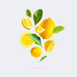 Juicy ripe flying yellow lemons, green leaves on light gray background. Creative food concept. Tropical organic fruit, citrus, vitamin C. Lemon slices. Summer minimalistic bright fruit background