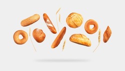 Various types of bread, ears of wheat flying on gray background. Classic wheat round bread, baguette, bun, sesame bagel. Organic Healthy Fresh isolated bread for bakery advertising. Food concept