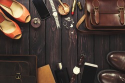 Top view, fashionable male and female personal items with space on a dark wooden background. Leather bag, shoes, watches, stylish accessories.