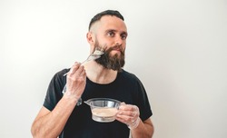 The charismatic guy hipster dyes his beard and hair on white background. Professional beard coloring. Bearded man, barber shop