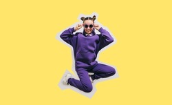 Cute teen girl in a purple casual sports suit hoodie and pants and white sneakers posing over yellow background. Mock-up for print.