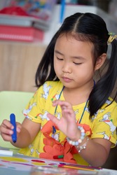 The girl happily drawing and painting on white paper. Asian girl sitting intently doing artwork on children's table.
