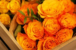 A bouquet of yellow orange roses with a green twig view from above in a wooden box in a flower shop. Rosa. 