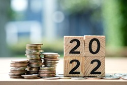 2022 NEW YEAR Business and saving money concept. Coins stack and wooden blocks number 2022 on blur background.