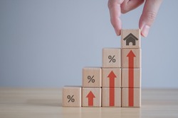Real estate concept. House, property investment, asset management, Interest rates, loan mortgage, house tax. Hand holding house icon on wooden block from stack of block with percent and rise of arrow.