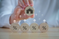 House and property investment and asset management concept. Interest rates, loan mortgage, house tax. Hand holding house icon on wooden circle from percent icon on wooden circle and rise of arrow.