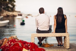Romantic couple on a date in nature,sitting on the bench looking at serene ocean scene.People living on the coast lifestyle.Fishing town couple dating.Fisherman life.Navy sailors relationship