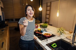 Young woman cooking a healthy meal in home kitchen.Making dinner on kitchen island.Preparing fresh meal,enjoying spice aromas.Eating in.Passion for cooking.Healthy lifestyle and dieting concept.
