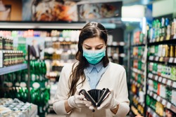 Worried woman with mask groceries shopping in supermarket looking at empty wallet.Not enough money to buy food.Covid-19 quarantine lockdown.Financial problems anxiety.Unemployed person in money crisis
