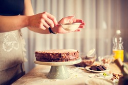 House wife wearing apron making finishing touches on birthday dessert chocolate cake.Woman making homemade cake with easy recipe,sprinkling  powdered sugar on top.Icing sugar sprinkled with colander