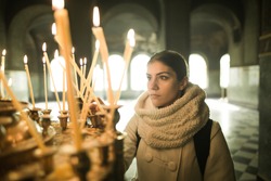 Young female lighting candles in a church during praying.Yellow votive candles burning.Woman praying to god at St. Alexander Nevsky Cathedral.Christianity.Strong christian religion faith
