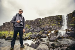 Young landscape photographer at waterfall at Pingvellir National Park.Photographing tectonic divide in Iceland between Eurasian and North American Continental plate and Oxararfoss fall in Thingvellir.