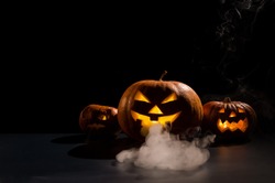 Halloween card. jack o lantern with candles glow on a black background. A row of creepy pumpkins with carved grimaces smokes in the dark.