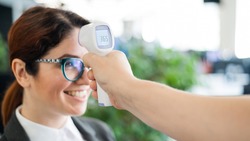 Temperature measurement by infrared electronic digital thermometer to all office workers. Happy woman in a business suit with an electronic thermometer near her forehead. Coronavirus Prevention