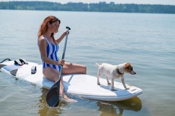 A woman is riding a surfboard with a dog