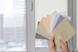 Woman holding fabric samples of roller blinds against window background. 