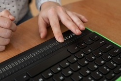 A blind woman uses a computer with a Braille display and a computer keyboard. Inclusive device.