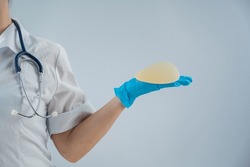 Female doctor aesthetic surgeon holding a breast implant on a white background. 