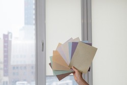 Woman holding fabric samples of roller blinds against window background. 