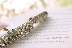 Flute, woodwind brass instrument in classical orchestra. Silver modern flute on white sheet music note for education and performance. Song composer on papers sway by wind.