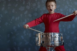 Teen boy in red suit playing drum in room. child holds drumsticks