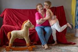 funny boy with glasses ran to his beloved grandmother who came to visit. Toy horse stands aside