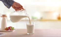 Serving breakfast milk with a jug in a glass on a white wooden kitchen table. Horizontal composition. Front view