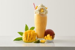 Mango milkshake with cream decorated with fruit around on white wooden table and light isolated background. Front view.