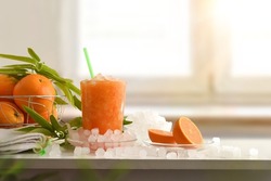 Detail of orange drink with a lot of ice on a white table with fruit and a bowl with ice around it. Front view. Horizontal composition.