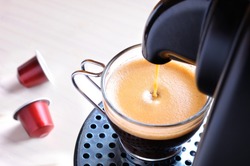 machine serving espresso coffee in a glass cup and two capsules on the table
