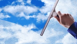 Employee hand cleaning a glass with rain drops and blue sky background.Concept and background window cleaning. horizontal composition