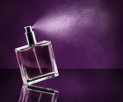perfume bottle spraying on dark purple background