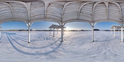 Winter full spherical seamless panorama 360 degrees angle view snow covered deserted beach with gazebos near lake  in snowy park with blue sky at evening in equirectangular projection. VR AR content