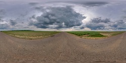 Full spherical seamless panorama 360 degree angle view on no traffic old asphalt road among fields with dark overcast sky before storm in equirectangular projection, VR AR content