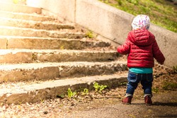 A baby walking on the street near the stairs