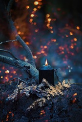 black burning candle in autumn mystery dark forest. witchcraft ritual. magic fall season natural background. Samhain sabbat, Halloween holiday concept