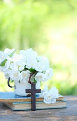 old biblical books, wooden cross and flowers on table in garden. symbol of Orthodox, Catholic, Protestant Christianity religion, faith in God, Church holiday concept. copy space