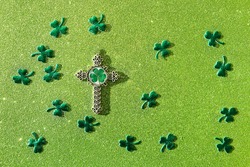 cross with Shamrock leaf and decorative clover leaves confetti on shiny green glittering background. symbol of st. Patrick, irish church holiday. saint Patrick's day festive concept. flat lay