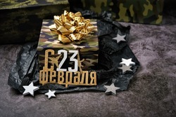 gift box with military camouflage pattern and golden bow, happy February 23 russian text on dark background. Present for day of defenders of fatherland. 23 february holiday. gift for man
