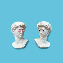 two antique copy Plaster sculpture heads with google eyes and pink hearts on eyes on blue background. modern style. creative minimal art concept. symbol of love, romance, Valentine's Day